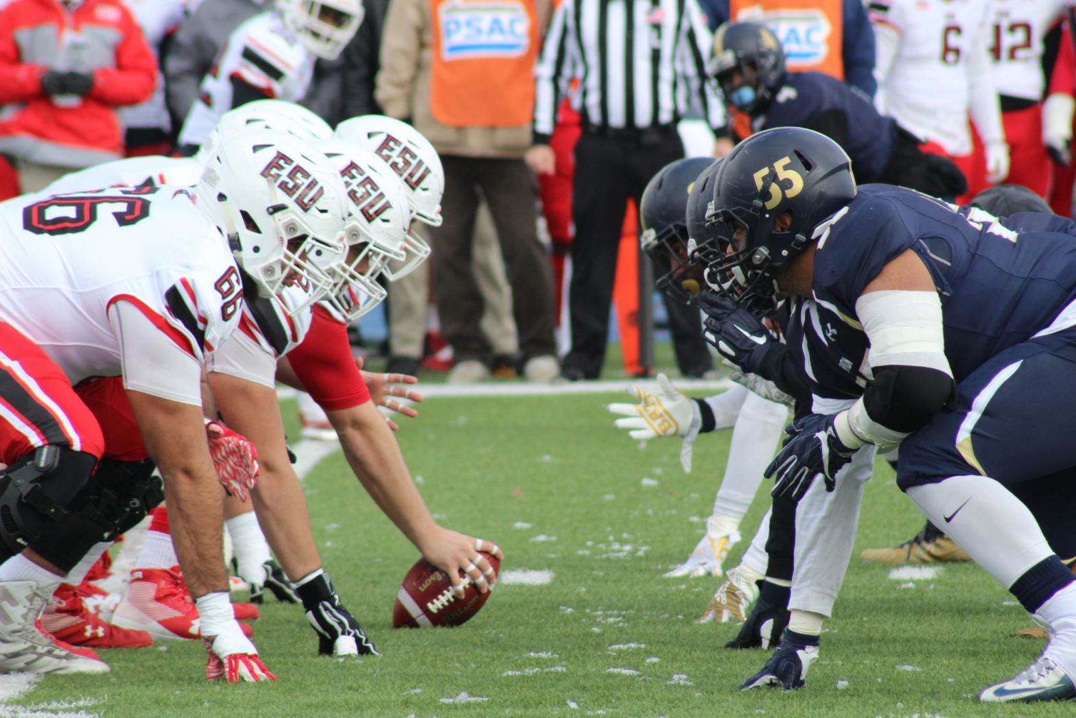 A closeup at field level shows two college football teams facing off, ready for the snap.