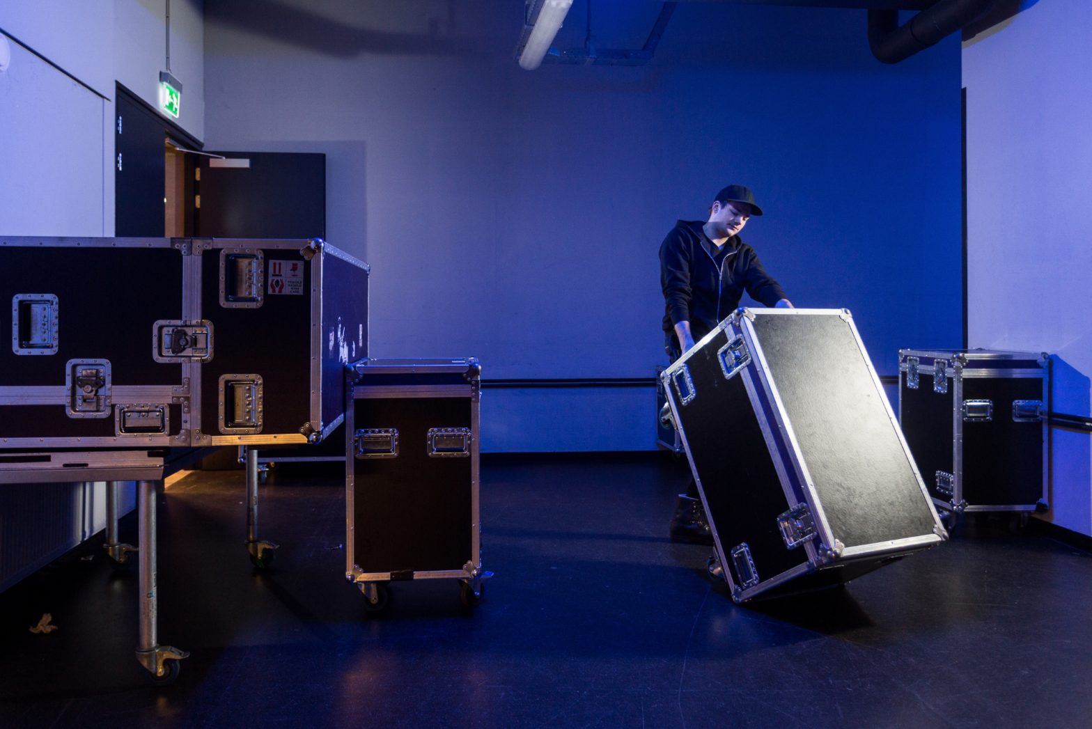 A member of a road crew rolls one case out of a room full of shockmount rack cases containing sensitive tech equipment.