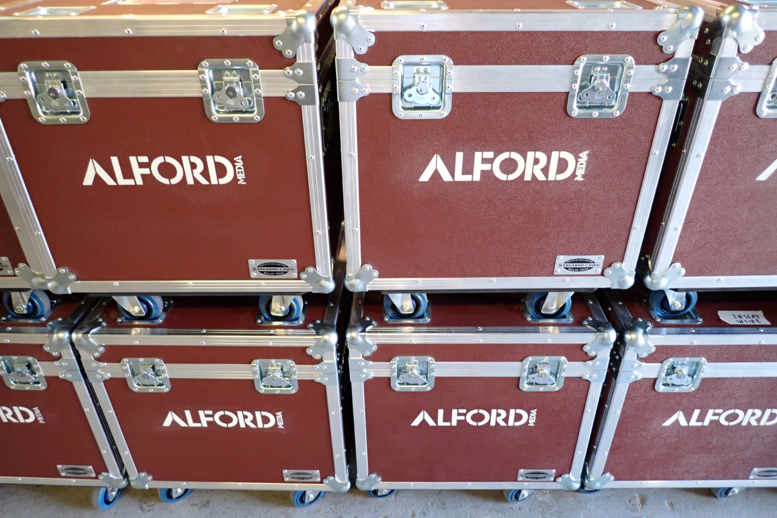 Stacks of custom maroon road cases are stenciled with a company’s white logo, enhancing their brand visibility.